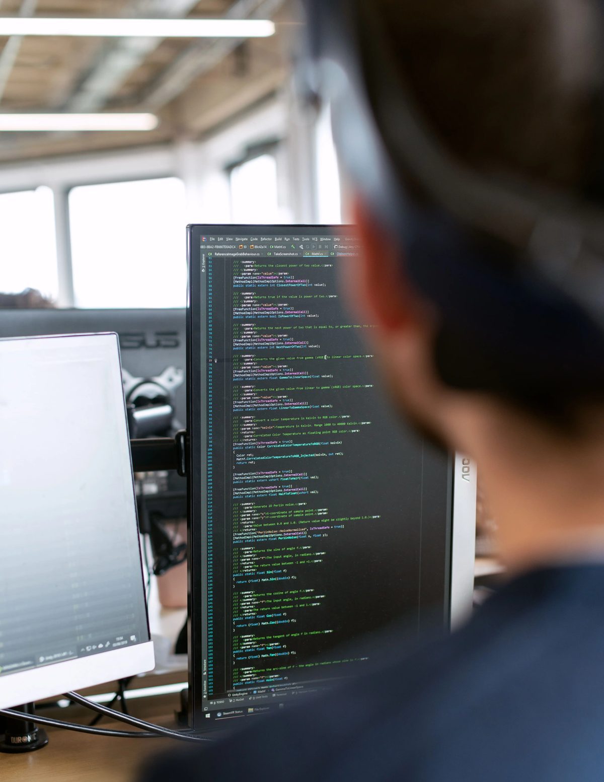 A developer working heads-down at dual monitors, headphones on